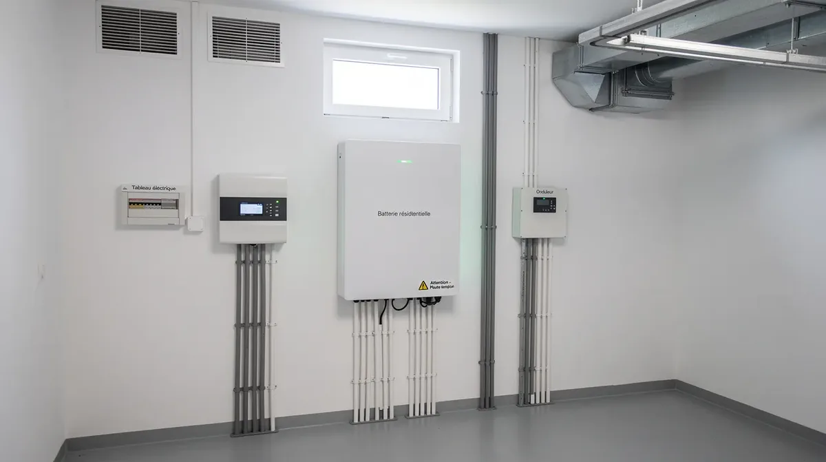 L'image montre une batterie résidentielle installée dans un local technique propre et bien ventilé, mettant en avant son système de stockage d'énergie. Cette batterie, conçue pour optimiser l'autoconsommation d'électricité produite par des panneaux solaires, illustre la technologie moderne de stockage, garantissant une durée de vie prolongée et une autonomie efficace.